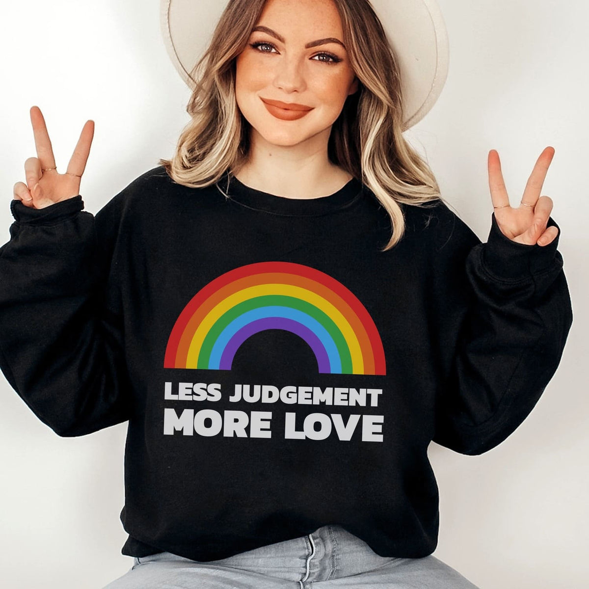 Person wearing a black pride sweatshirt with a rainbow and text design, making peace signs.
