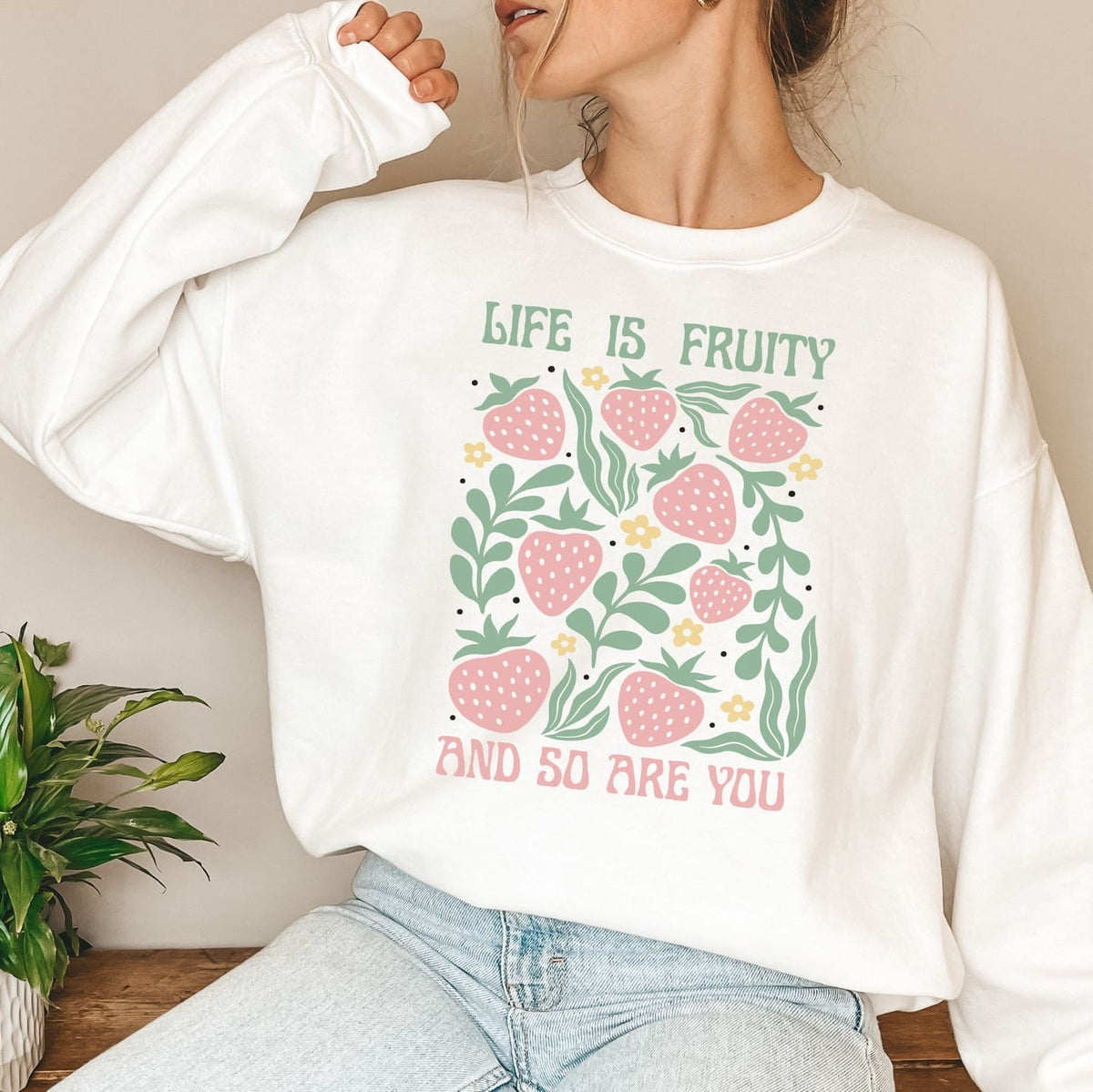 Person wearing a white sweatshirt with a fruity queer strawberry design and text.
