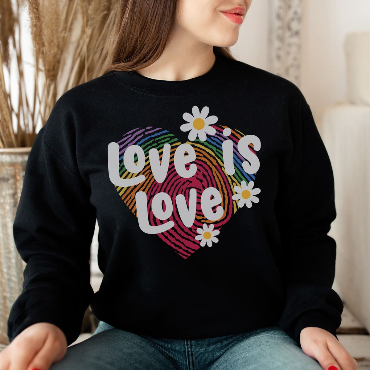 Person wearing a black lgbt pride sweatshirt with 'Love is Love' rainbow heart design.