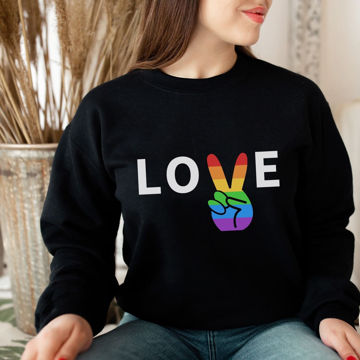 Person wearing a black sweatshirt with 'LOVE' and rainbow pride hand design.