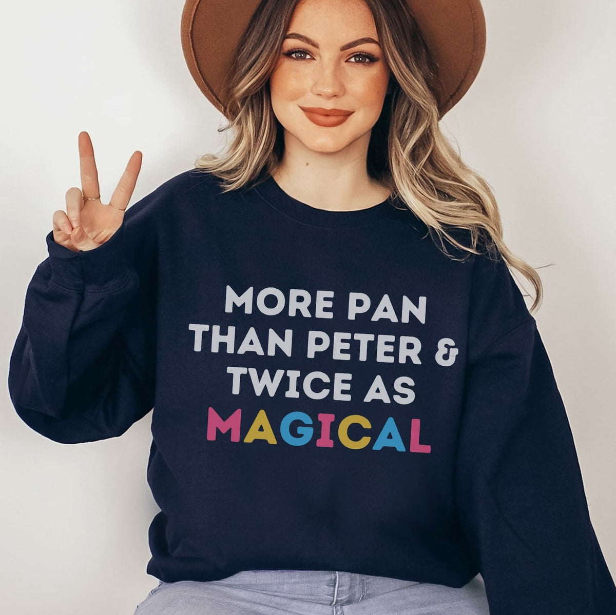 Person wearing a navy pansexual sweatshirt with colorful text, making a peace sign.