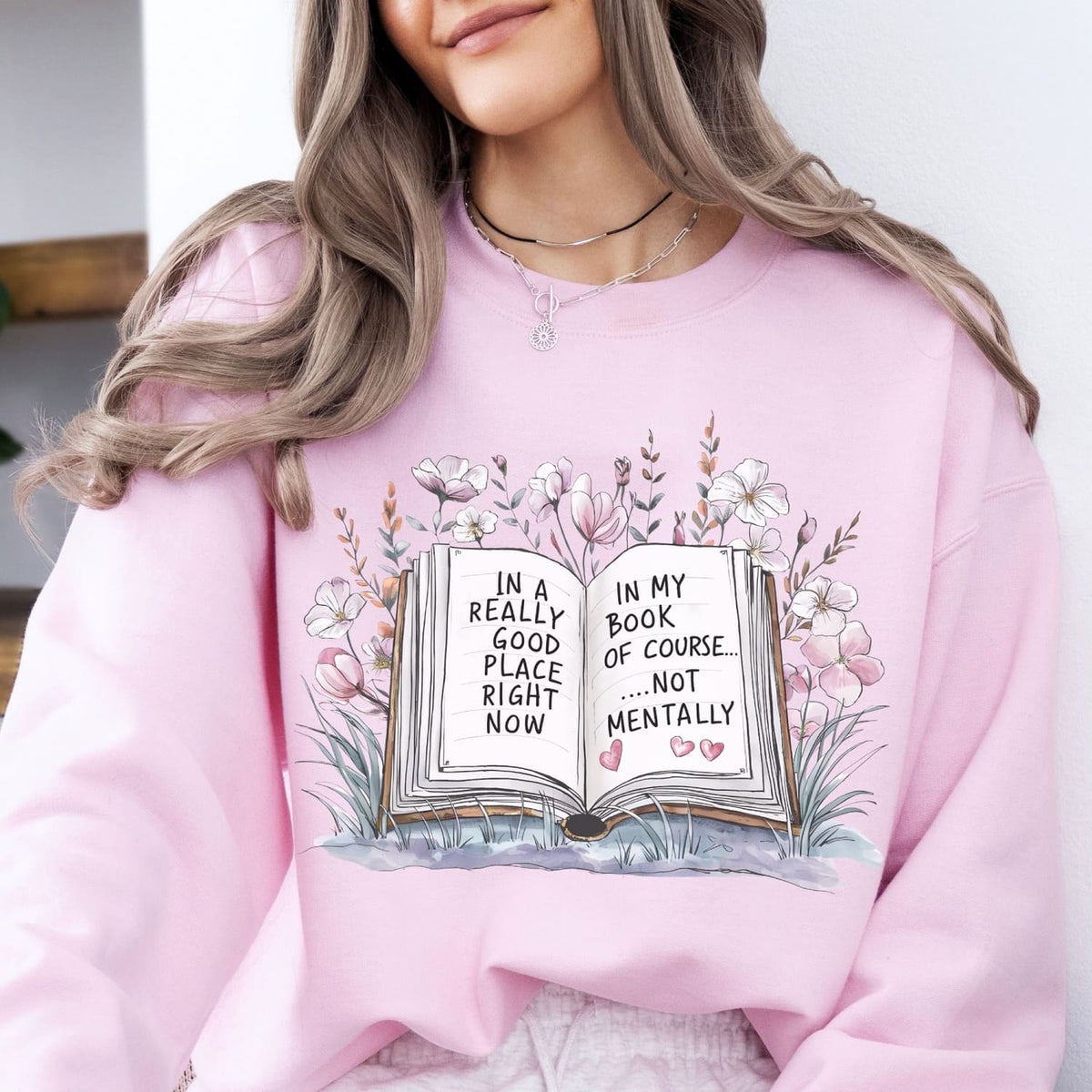 Person wearing a pink mental health sweatshirt with a book graphic and text.