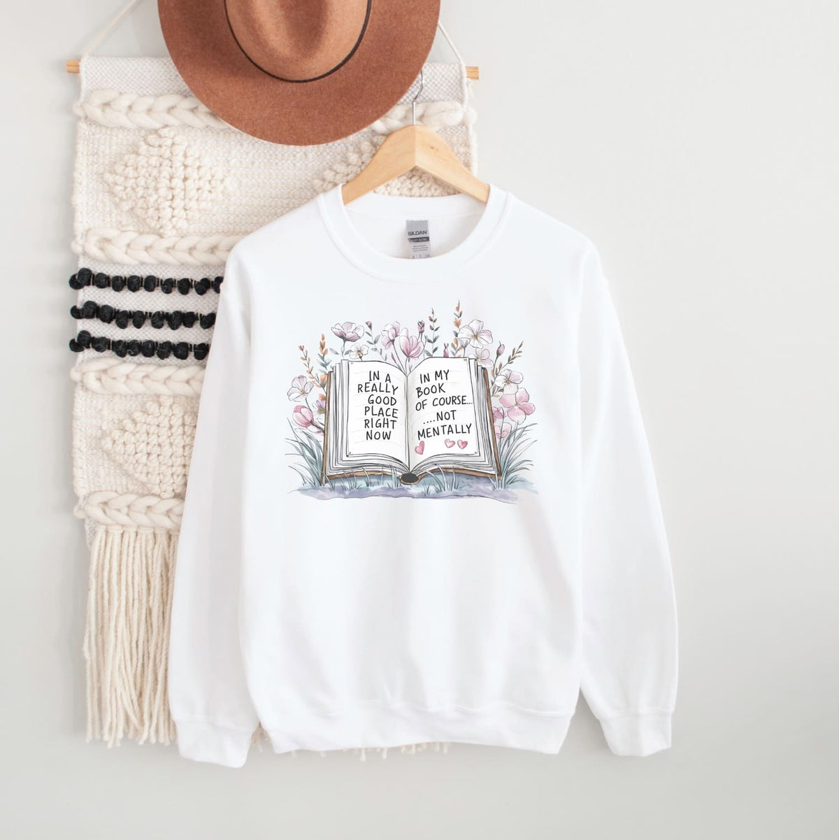 White bookish mental health sweatshirt with a graphic design on a hanger against a white background