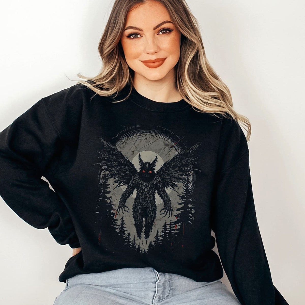 Woman wearing a black sweatshirt with mothman graphic design on a plain background