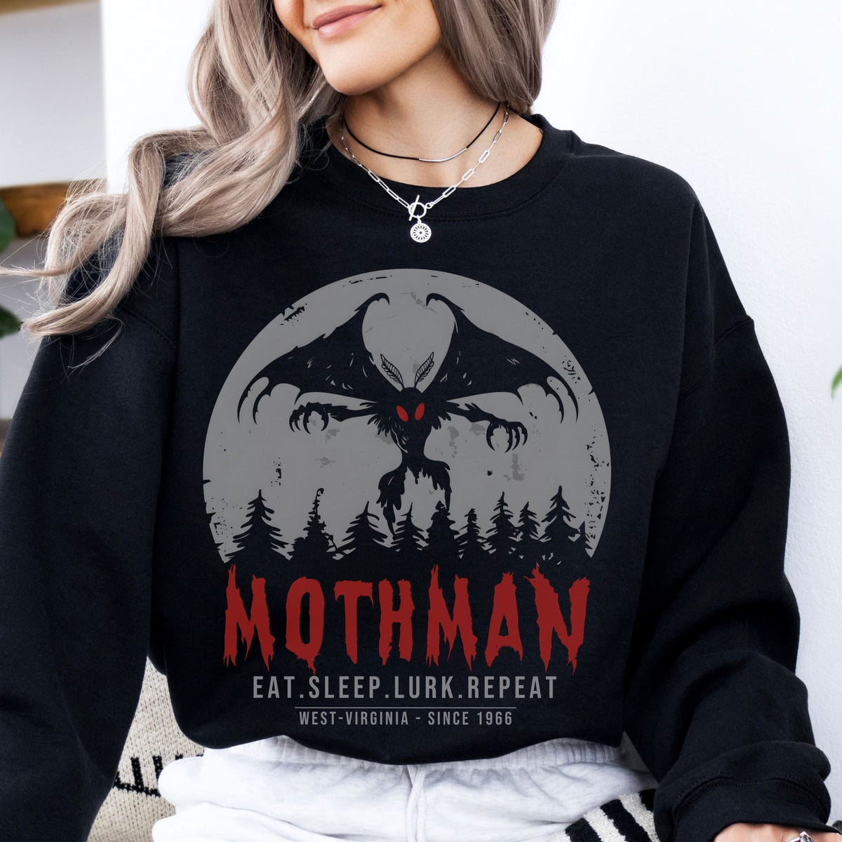 Person wearing a black sweatshirt with Mothman graphic and text