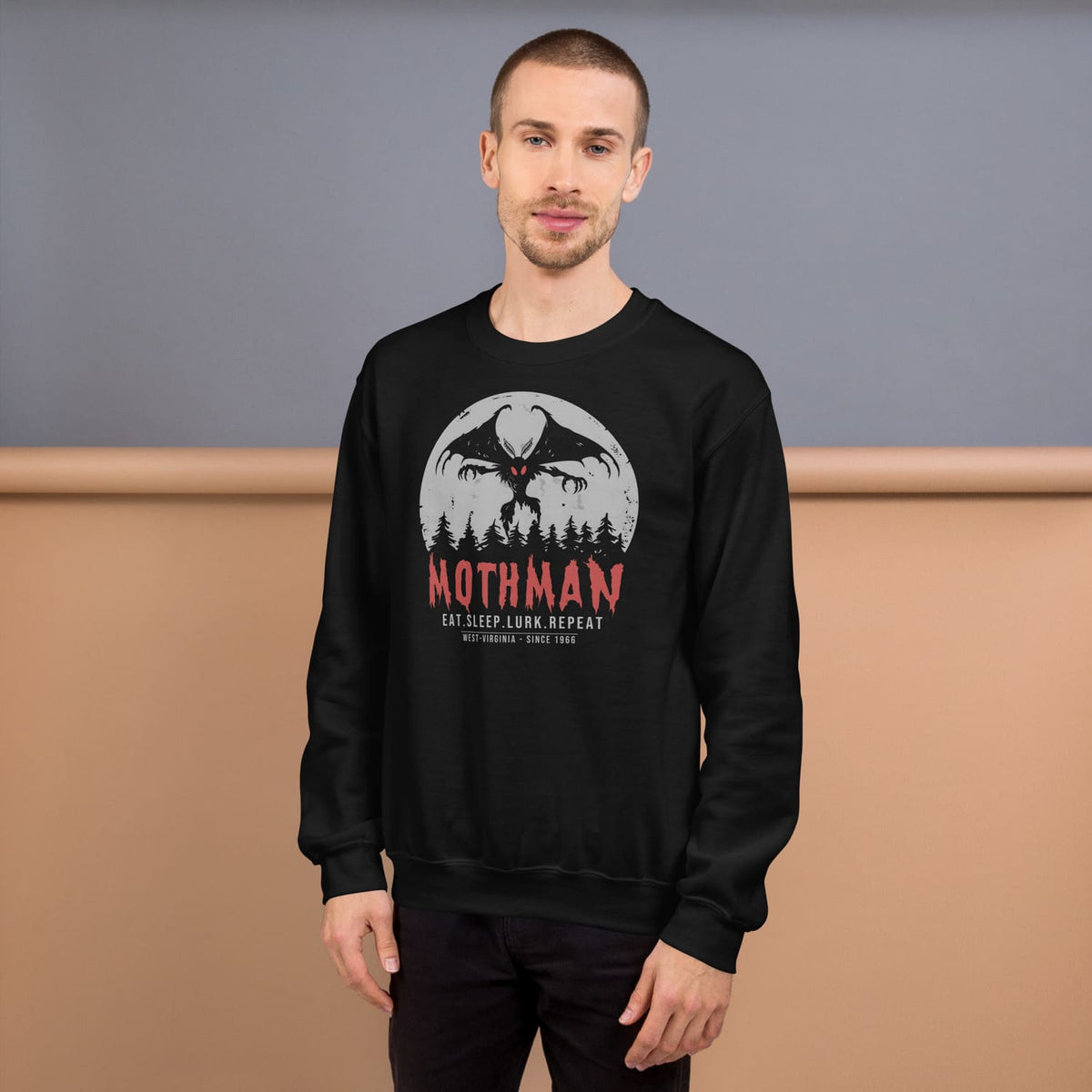Person wearing a black sweatshirt with Mothman graphic and text