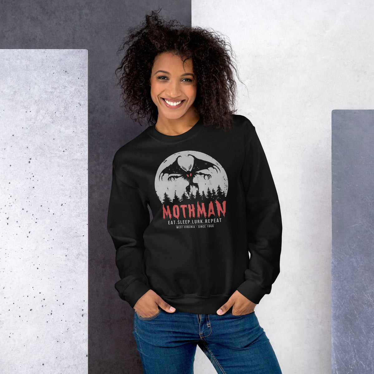 Woman wearing a black sweatshirt with Mothman graphic design against a gray and white background