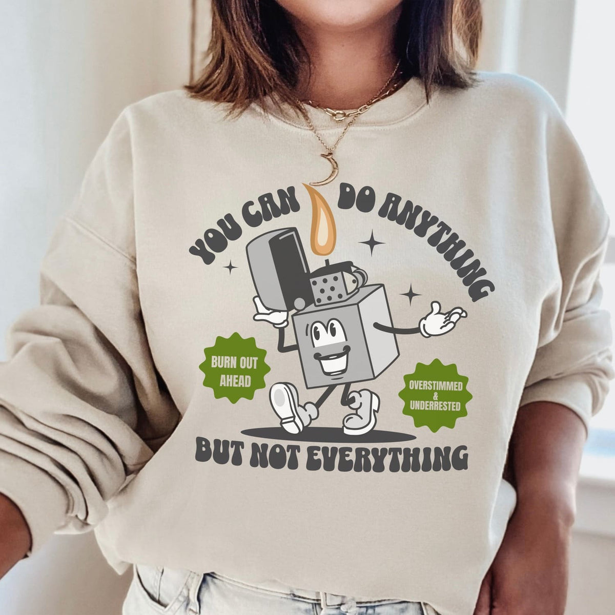 Beige burnout sweatshirt with cartoon design and motivational text worn by a person.