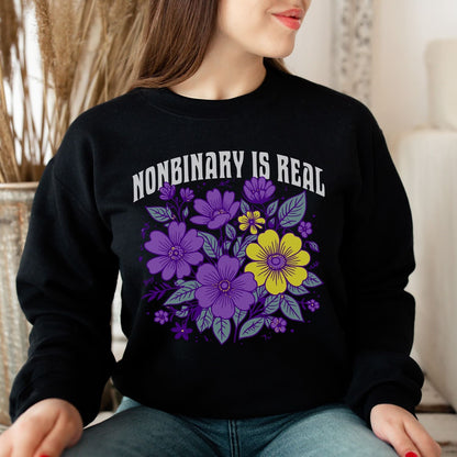 Person wearing a black sweatshirt with floral design and 'NONBINARY IS REAL' text.