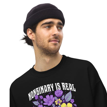 Person wearing a black sweatshirt with 'Nonbinary is Real' text and floral design on a white background
