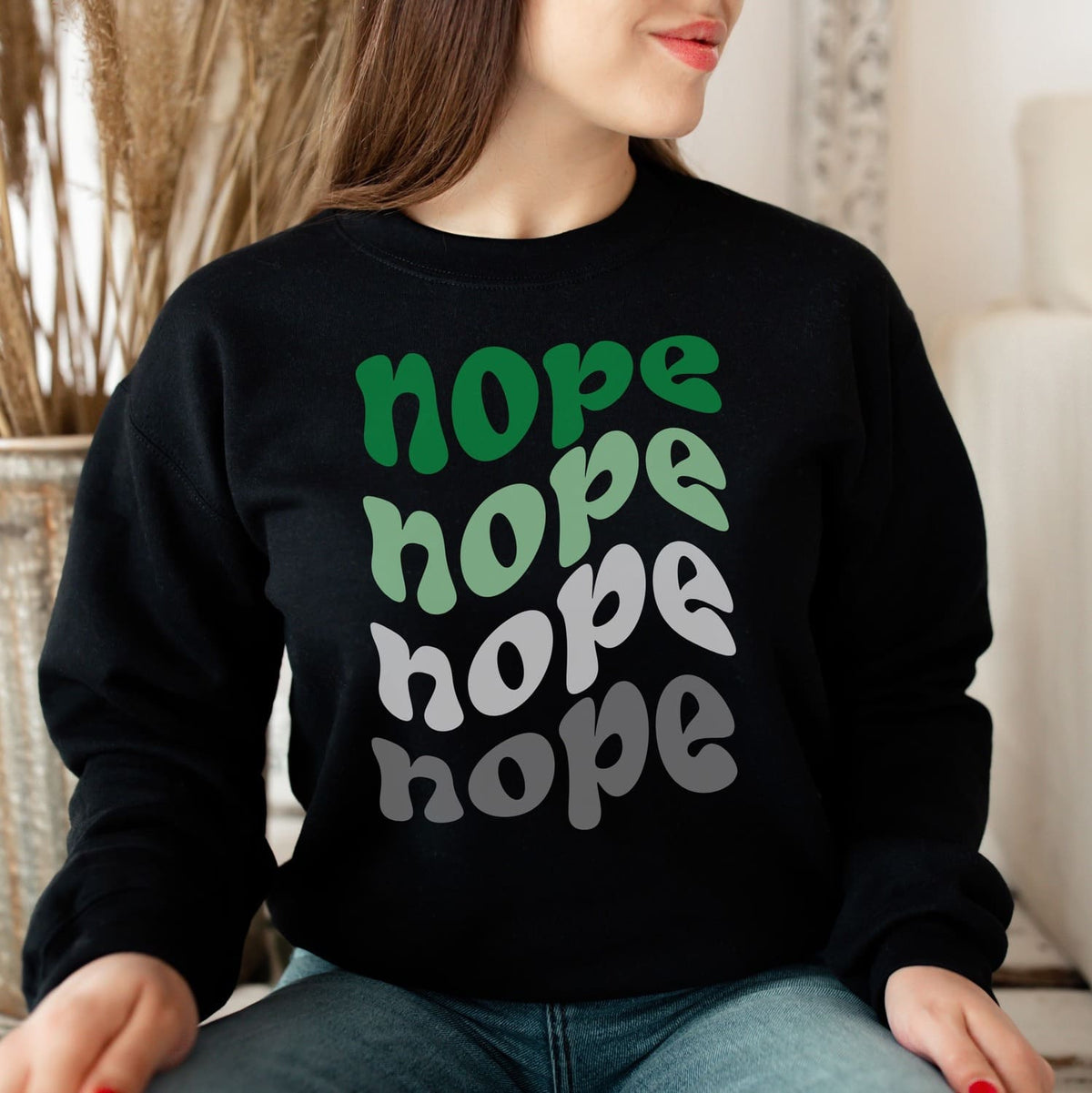 Person wearing a black aromantic sweatshirt with 'nope' text in multiple colors.