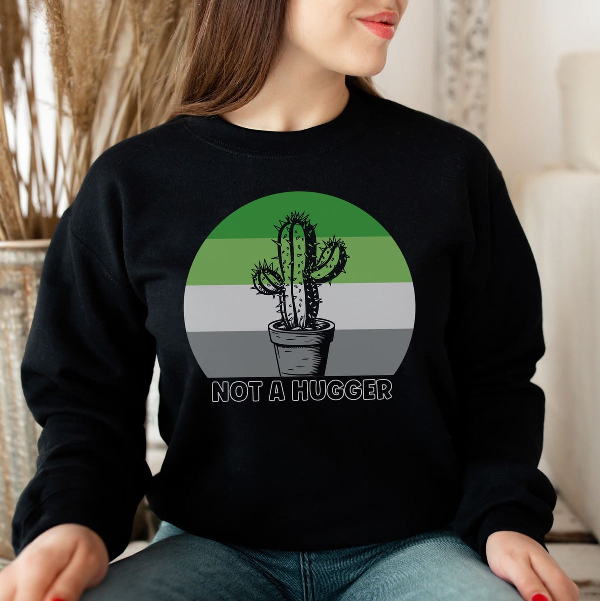 Person wearing a black aromantic sweatshirt with a cactus graphic and 'Not a Hugger' text.
