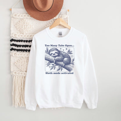 White sweatshirt with overstimulated sloth graphic and text on a hanger with a hat and macramé wall in the background