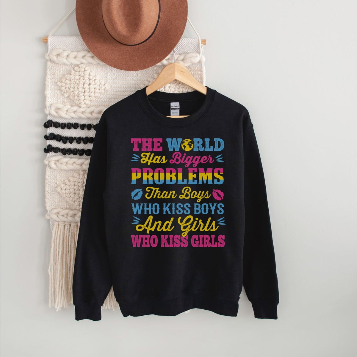 Black pansexual sweatshirt with colorful text on a hanger against a white wall.