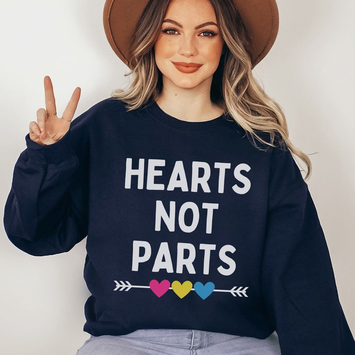 Person wearing a navy pansexual pride  sweatshirt with 'Hearts Not Parts' text and colorful hearts design.