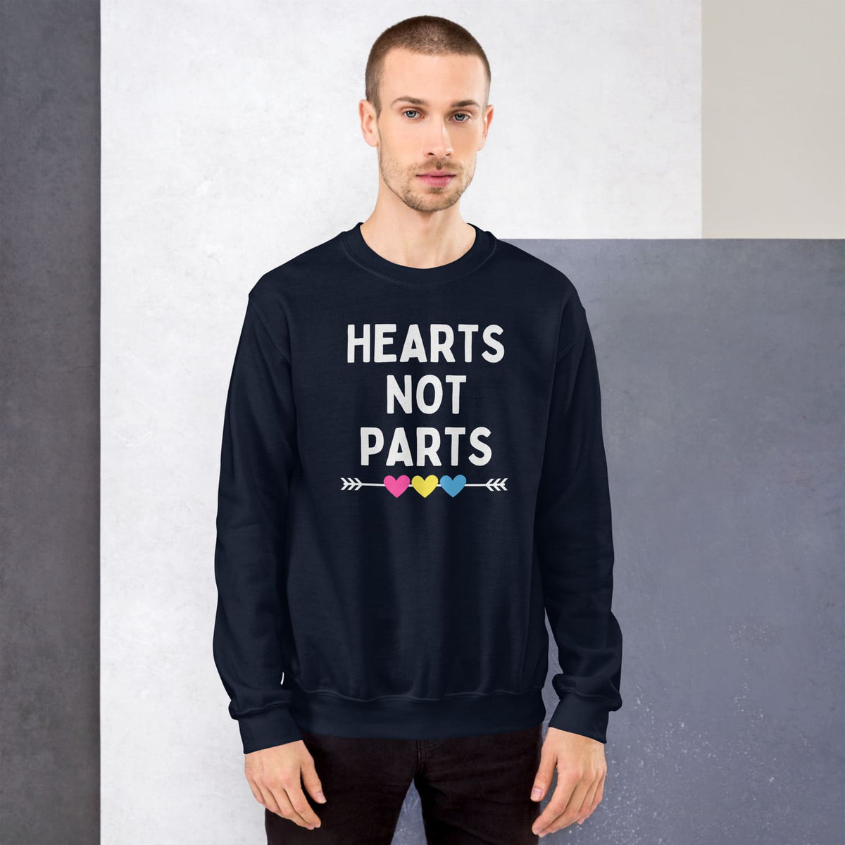 Pansexual person wearing a sweatshirt with 'HEARTS NOT PARTS' text and colorful hearts design.