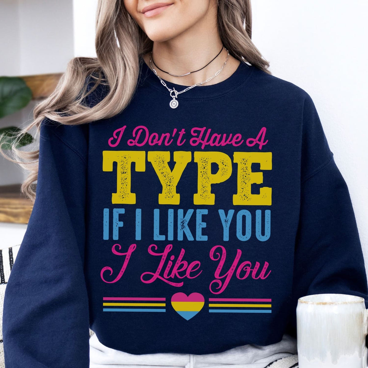 Person wearing a navy pansexual sweatshirt with colorful text and a heart symbol.