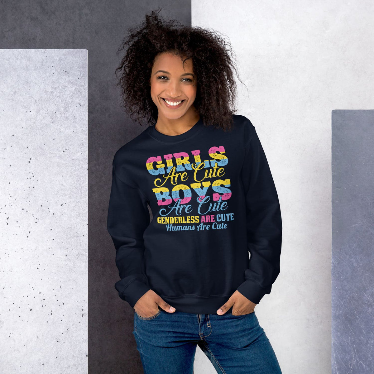 Woman wearing a navy pansexual sweatshirt with colorful text standing against a gray and white wall.