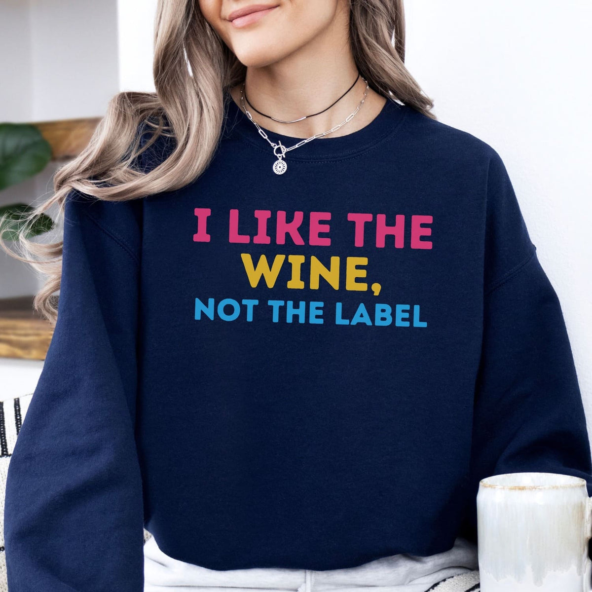 Person wearing a navy blue pansexual sweatshirt with colorful text 'I LIKE THE WINE, NOT THE LABEL'.