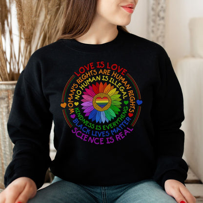 Person wearing a black pride sweatshirt with colorful text and symbols on a blurred indoor background