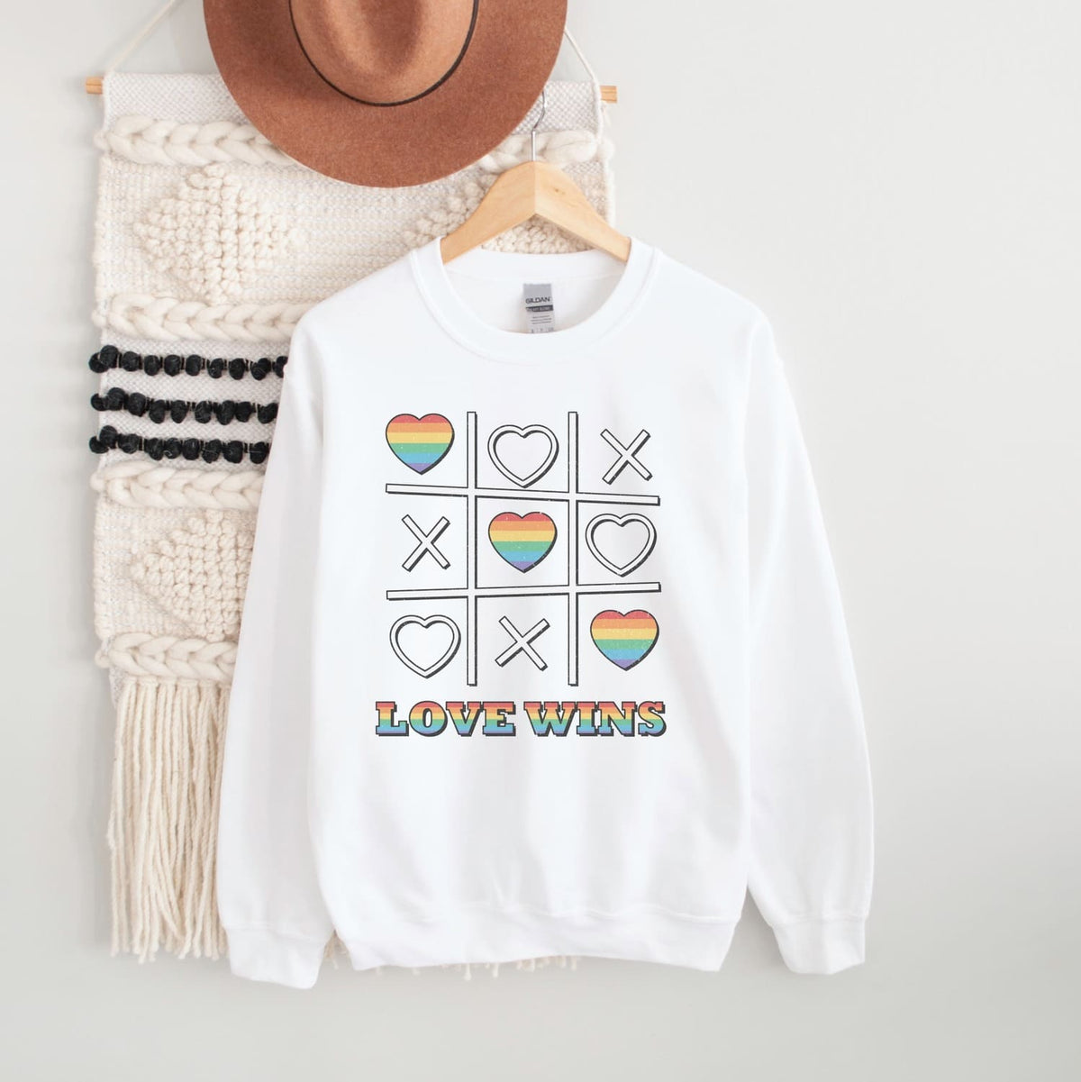 White pride LGBTQ sweatshirt with rainbow heart and cross design, 'LOVE WINS' text, on a white background.