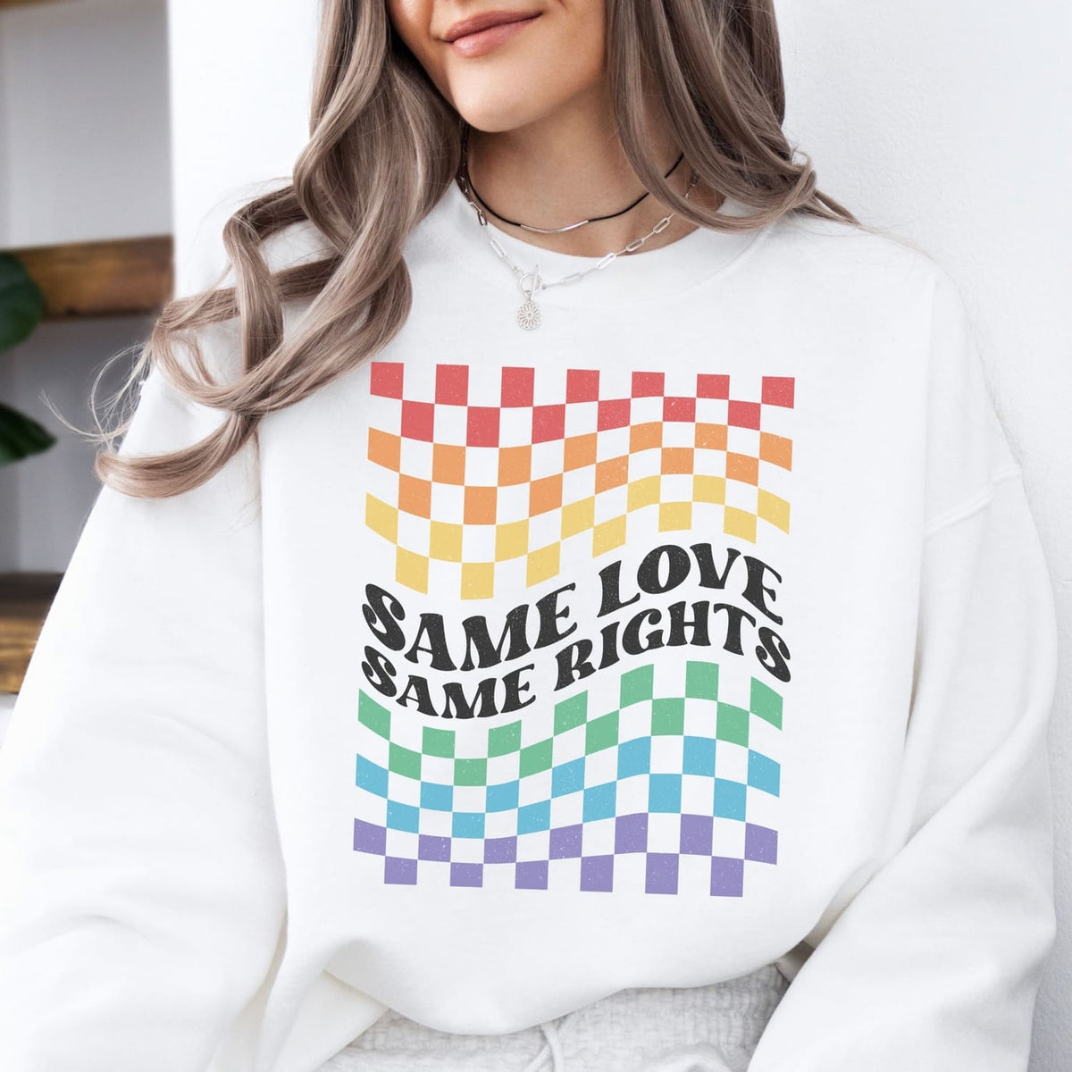 Person wearing a white LGBTQ pride sweatshirt with rainbow checkered design and 'Same Love Same Rights' text