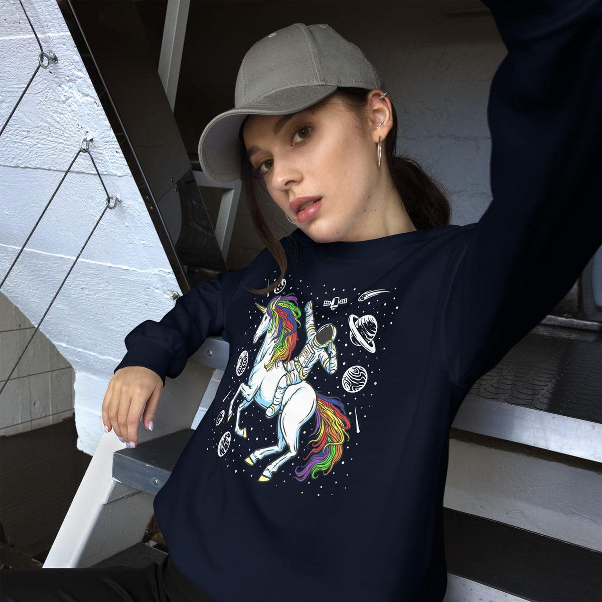 Person wearing a navy sweatshirt with a rainbow lgbtq unicorn design, sitting on stairs. 