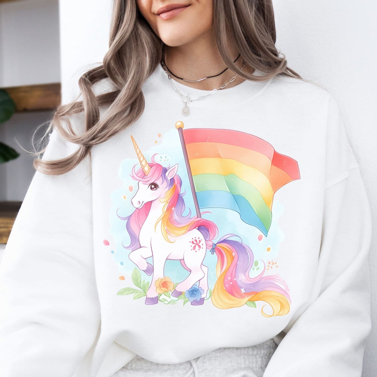 Person wearing a white lgbtq sweatshirt with a colorful unicorn design holding a rainbow pride flag.