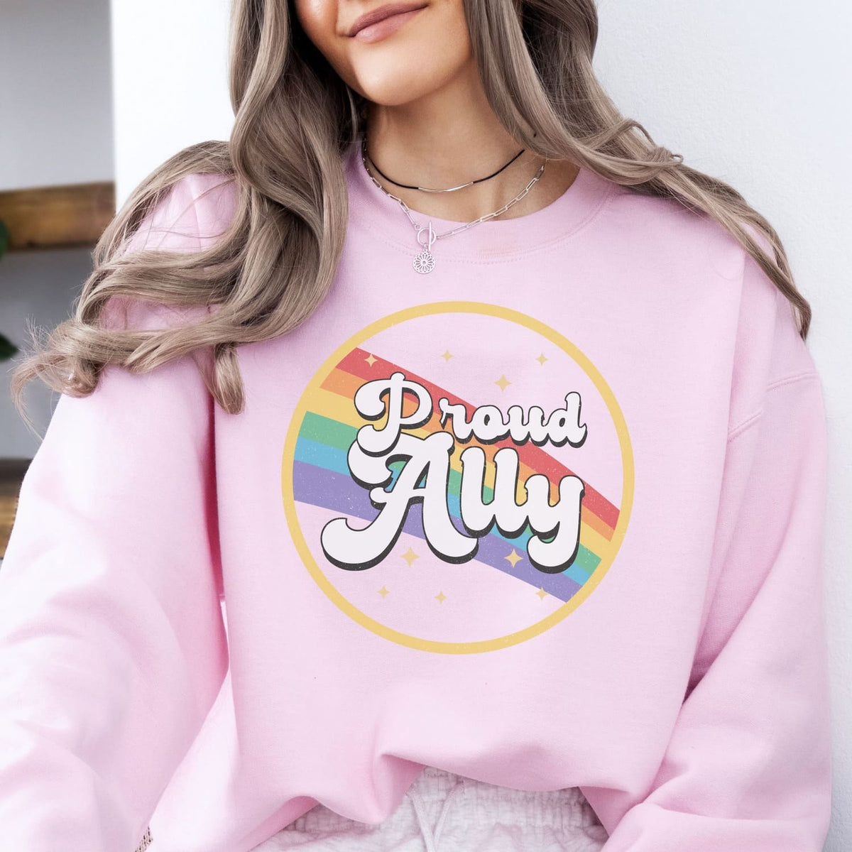 Person wearing a pink ally pride sweatshirt with a rainbow and text design.