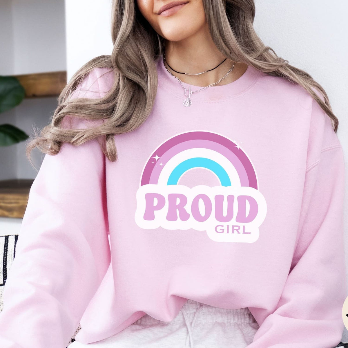 Person wearing a pink sweatshirt with a rainbow and 'PROUD GIRL' text design.