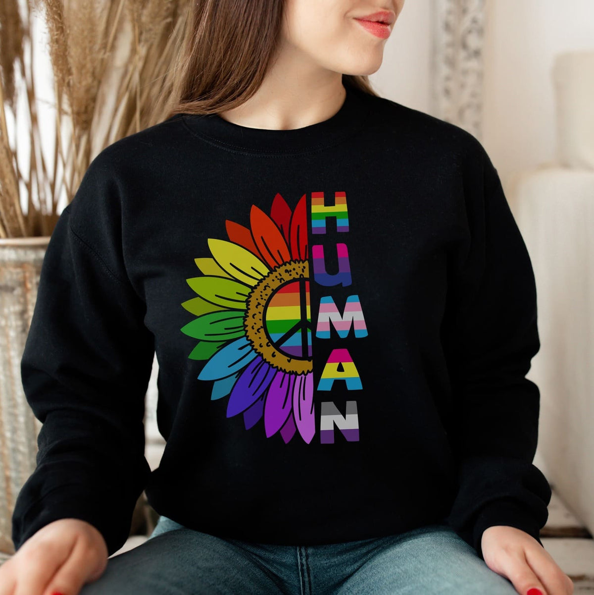 Person wearing a black pride LGBT sweatshirt with a colorful 'HUMAN' design featuring a rainbow flower and peace symbol.