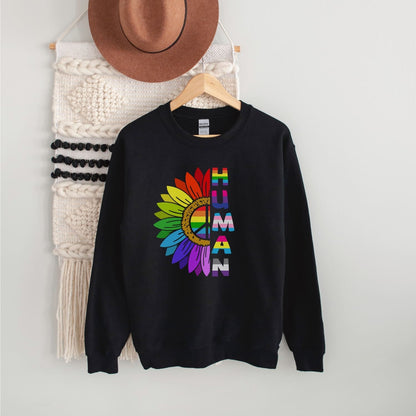 Black LGBTQ pride sweatshirt with rainbow sunflower design and 'HUMAN' text on a hanger against a white wall.