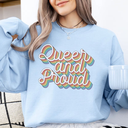 Person wearing a light blue pride sweatshirt with 'Queer and Proud' text in rainbow colors, holding a white mug.