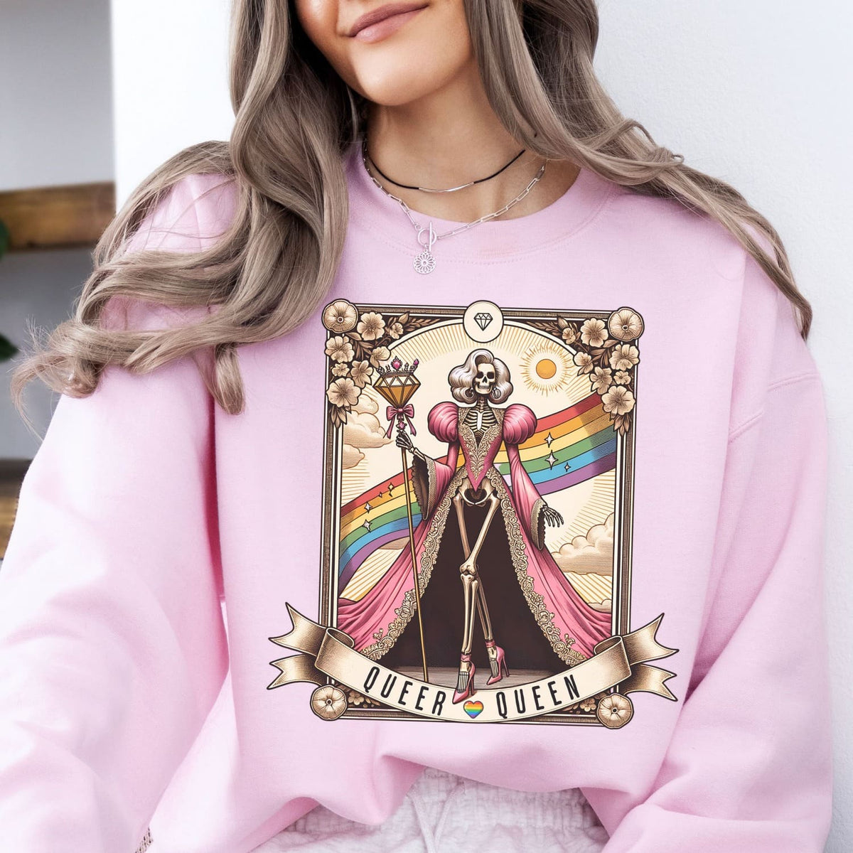 Person wearing a pink sweatshirt with a Queer Queen design featuring a skeleton holding a rainbow flag.