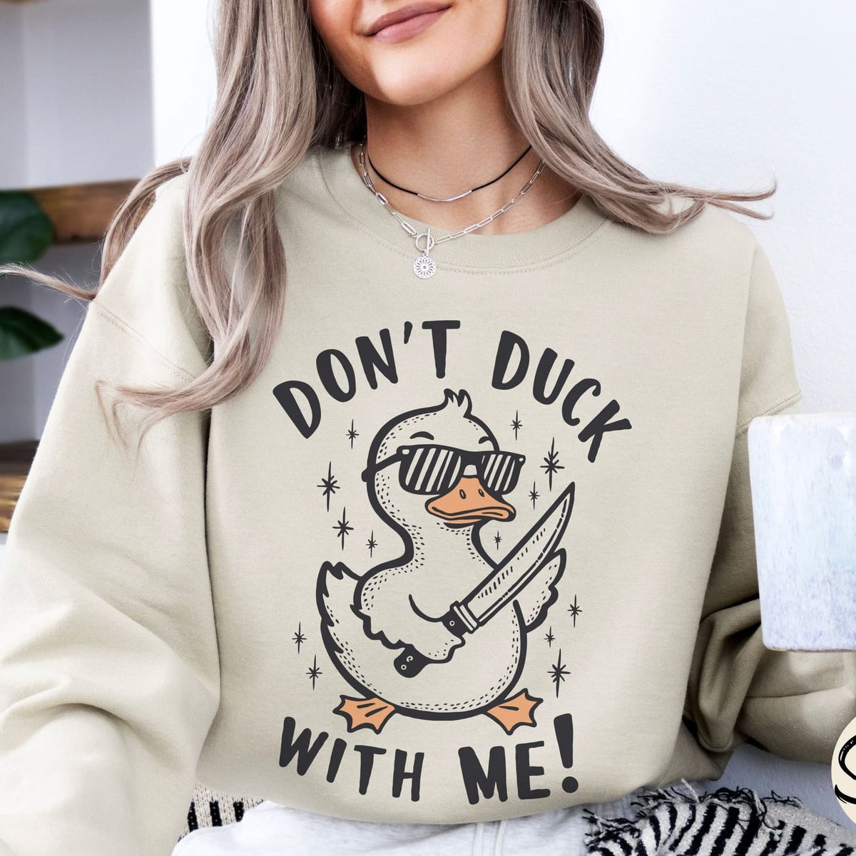 Person wearing a beige funny  sweatshirt with a graphic design and text 'Don't Duck With Me!'
