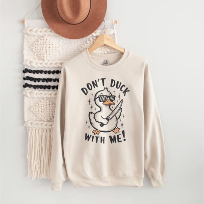 Beige sweatshirt with a funny duck graphic design and text, hanging on a wooden hanger against a white wall.