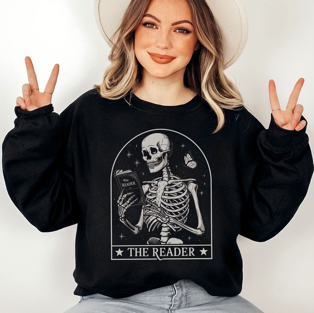 Person wearing a black sweatshirt with a skeleton design and 'The Reader' text, making peace signs.