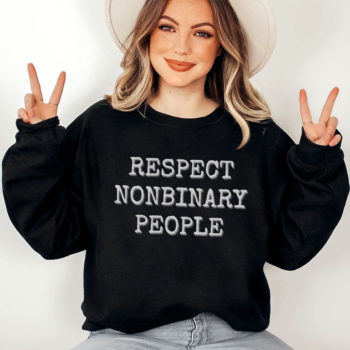 Person wearing a black sweatshirt with 'RESPECT NONBINARY PEOPLE' text, making peace signs.