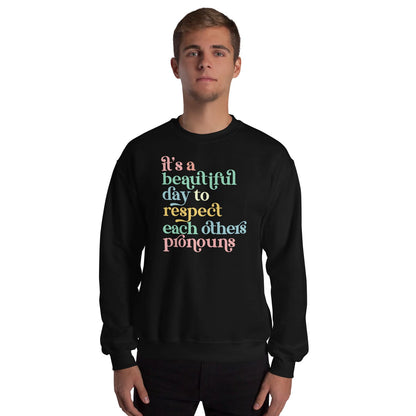 Person wearing a black pronouns sweatshirt with colorful text on a white background