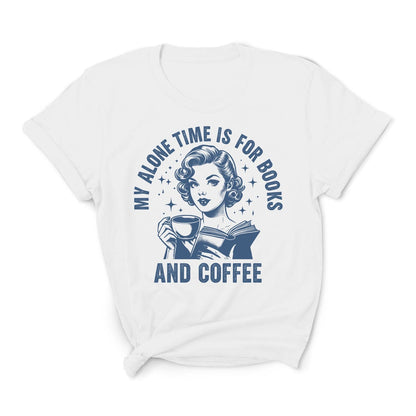 White t-shirt with a graphic of a woman reading a book and holding a coffee cup, with text 'My alone time is for books and coffee' on a white background.