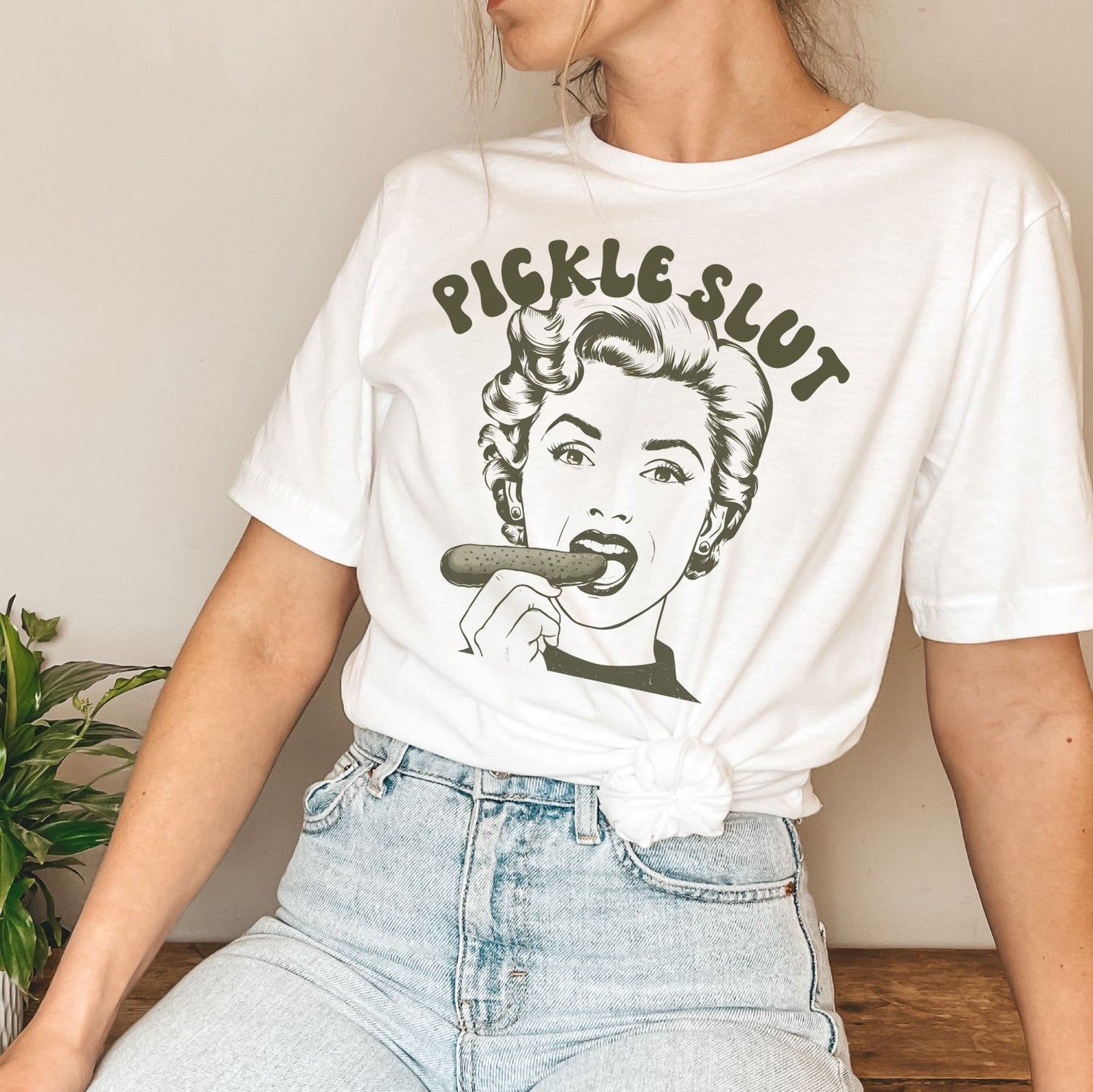 Person wearing a white t-shirt with a graphic design and text pickle slut.