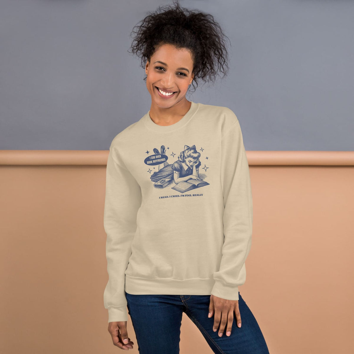 Woman wearing a beige sweatshirt with a bookish graphic design, standing against a plain background