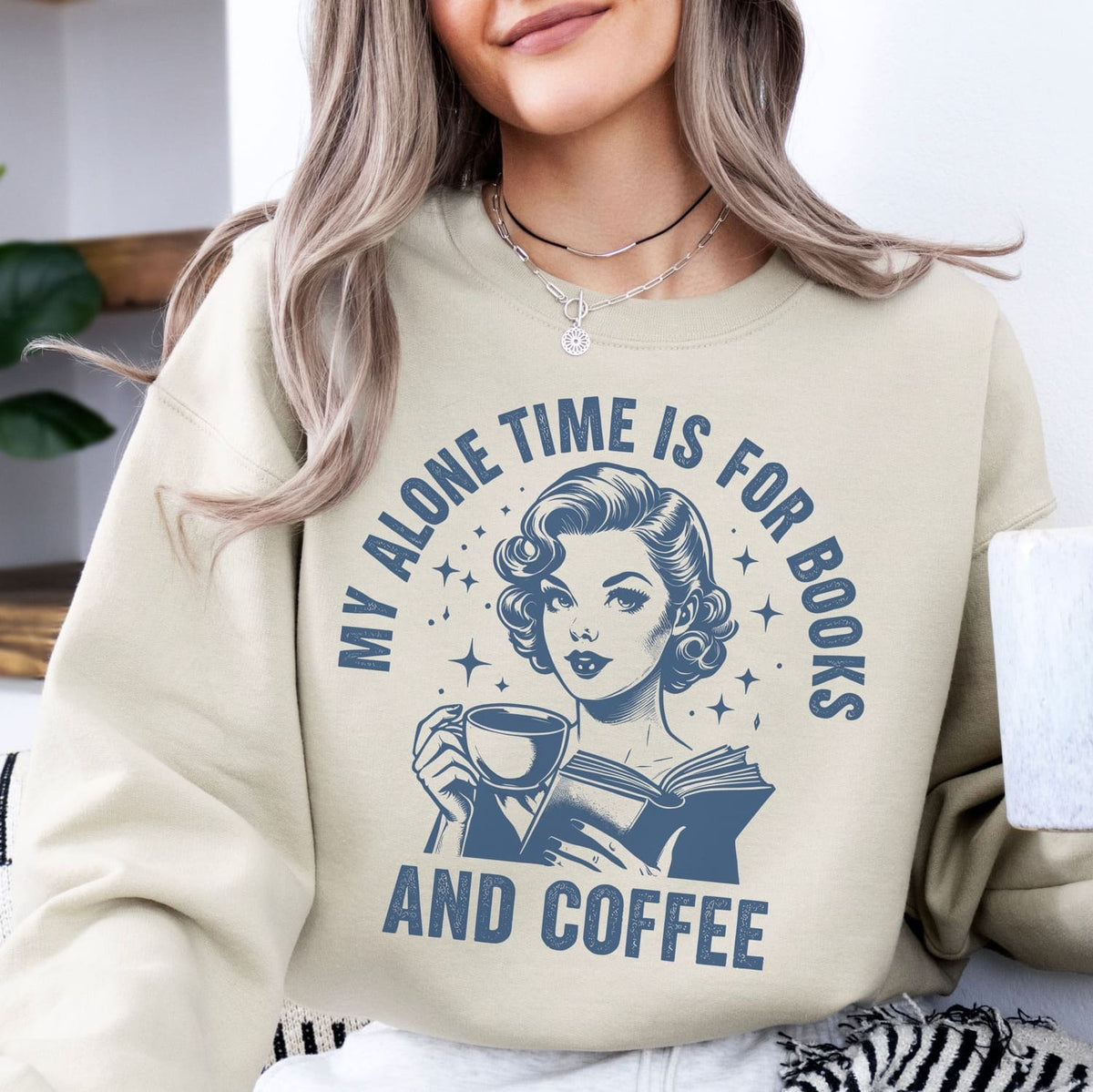 Person wearing a beige sweatshirt with a graphic and text 'My alone time is for books and coffee'.
