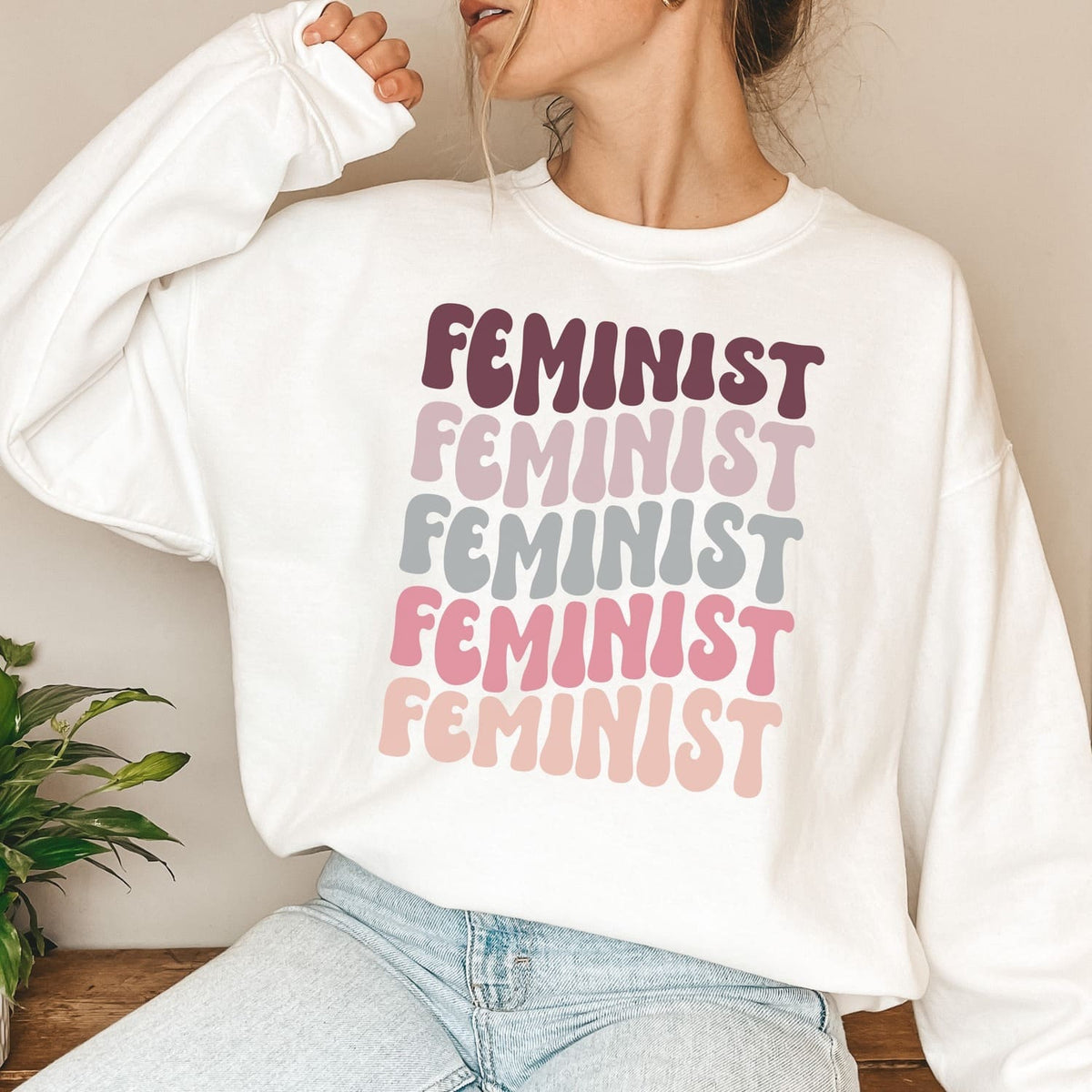 Person wearing a white sweatshirt with 'FEMINIST' text in various colors.