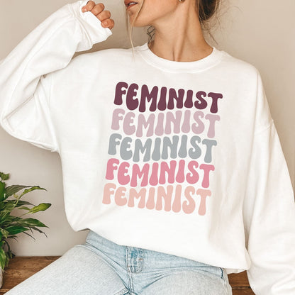 Person wearing a white sweatshirt with 'FEMINIST' text in various colors.