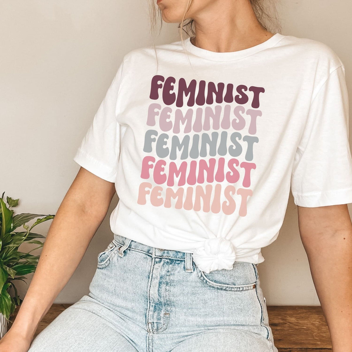Person wearing a white t-shirt with 'FEMINIST' printed multiple times in different colors.