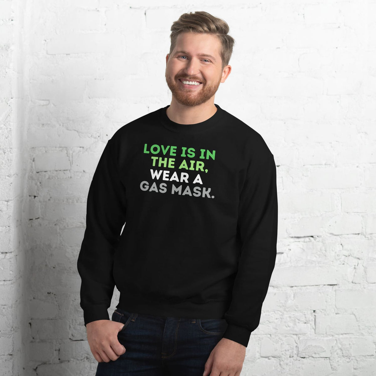Man wearing a black aromantic sweatshirt with a humorous message against a white brick wall.