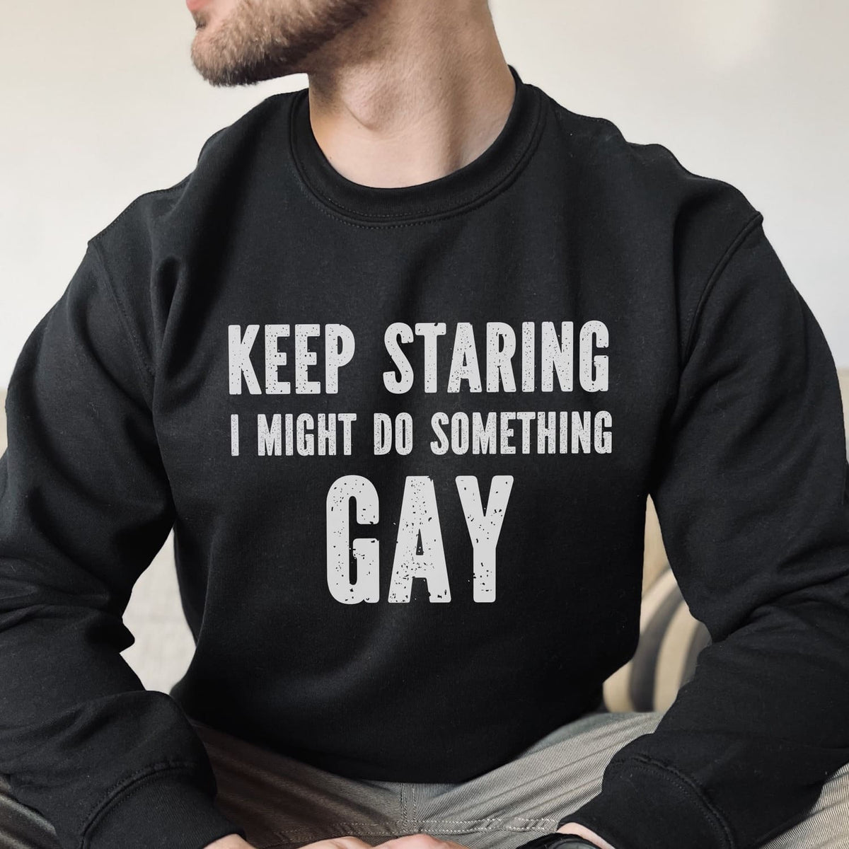 Person wearing a black sweatshirt with text 'KEEP STARING I MIGHT DO SOMETHING GAY' on a neutral background