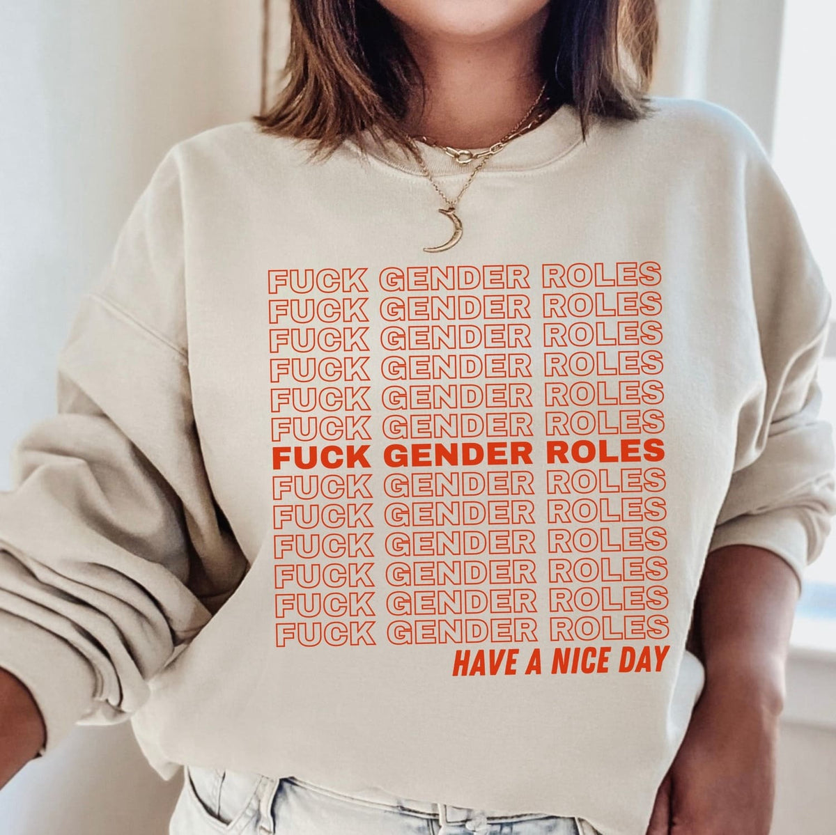 enby Person wearing a beige sweatshirt with red text stating 'FUCK GENDER ROLES' repeated multiple times, followed by 'HAVE A NICE DAY'.