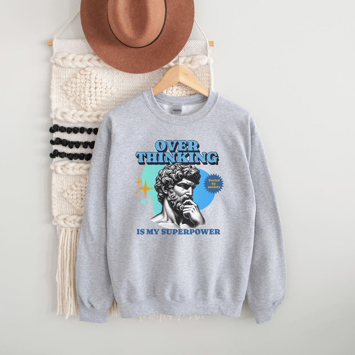 Gray anxiety sweatshirt with a graphic design and text, hanging on a wooden hanger against a white background.